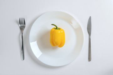 Knife, fork and yellow pepper, paprica on a white plate on a white background, top view