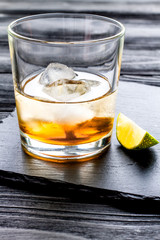 rum with ice in glass on dark background and lime