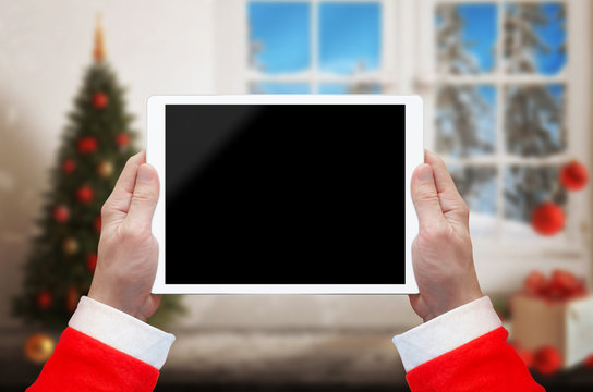 Santa Claus work on tablet with isolated screen for interface promotion. Christmas time with decorations.