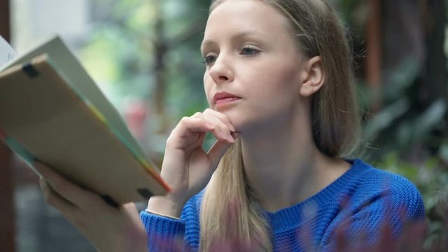 Girl stops reading book because of the headache, steadycam shot
