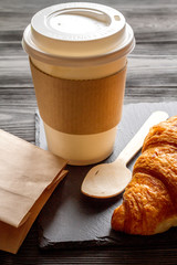 cup coffee and croissant in paper bag on wooden background