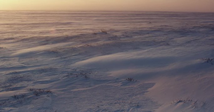 Pan towards setting sun over snow blown frozen tundra