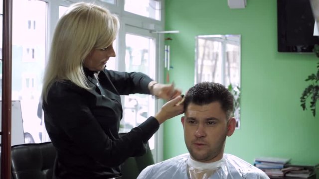 Haircut at hairdresser's. Beautiful blonde woman cutting men's dark hair. HD