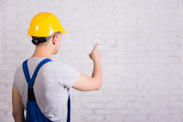 back view of man in blue builder uniform pointing at white wall
