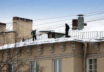 Fototapeta na wymiar Take off the snow and icicles from the roof. Working cleaning work without insurance. Russia, St. Petersburg