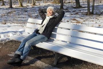 Fototapeta premium The young beautiful woman has a rest on a bench in the winter park..