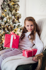 Fototapeta na wymiar Happy child girl sitting on armchair covered with a blanket against decorated christmas fireplace