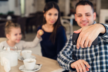 family, parenthood, technology people concept - happy mother, father and little girl having dinner taking selfie by smartphone at restaurant
