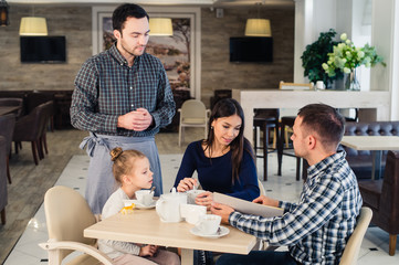 restaurant and holiday concept - waiter giving menu to happy family at cafe