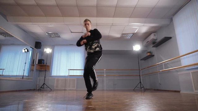 Young man dancing break dancing professionally in the dance studio. Dancer actively moving his arms. Boy with a serious expression on his face.