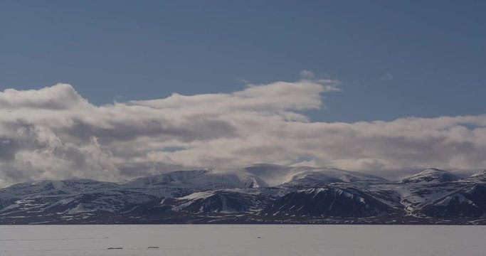 Time lapse - clouds race over snowy mountains across sea ice