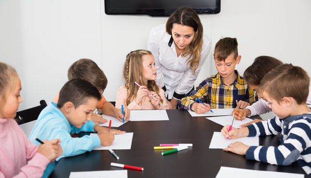 Little children with speaking teacher drawing in classroom