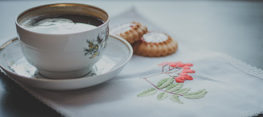 Cup of tea and a biscuit on a napkin with an embroidered branch of Rowan