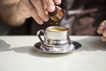 silver cup of coffee with a man's hand pouring cream milk