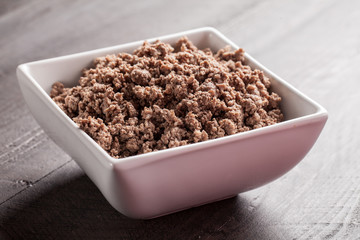 Small white bowl of cooked ground meat on brown wooden table