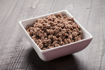 Horizontal shot of small white bowl of cooked ground meat on brown wooden table