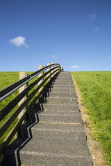 Obraz premium A concrete staircase with wood banister between the green grass of a dike on a sunny day