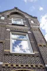 Facade of a Dutch red brick house with reflection of sky and clouds in the big windows