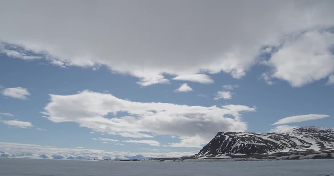 Time lapse - Clouds race over mountain spit over sea ice on sunny day