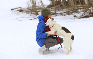 Young woman with her dog on the snow in winter.Girl hugging dog.Woman outdoors with her cute dog having fun./Girl with dog in winter park
