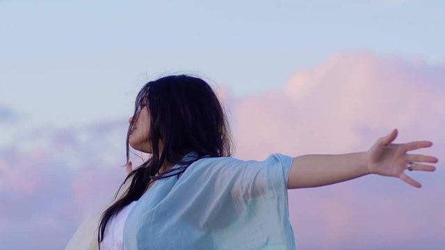 relaxing young woman opens arms to the sky suggestive clouds in background