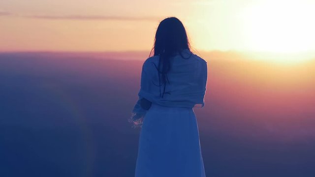 woman on the top of a mountain is viewing  plain in front of her at the sunset