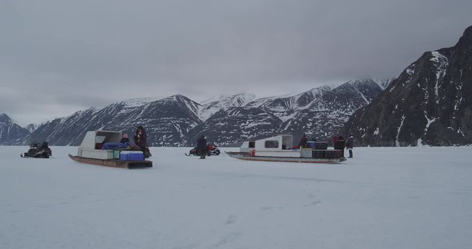 Skidoos Komatiks and Tourists on sea ice with Mountains