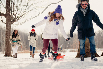 Group of friends enjoying pulling a sled in the snow in winter