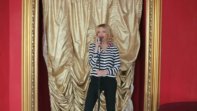 Beautiful singing girl in karaoke. Beauty woman with retro microphone. Girl in black pants and striped shirt on a gold background.