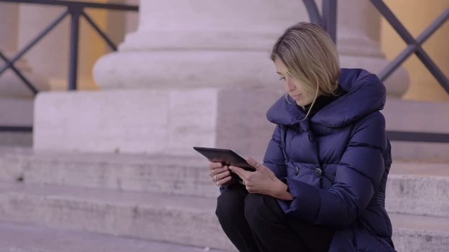 young woman using tablet pc sitting on the stairs of St. Peter square in Rome