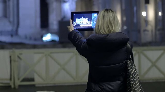 young woman is making photos to St. peter church in the night with tablet pc