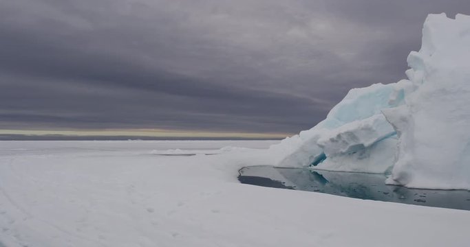 Pan from skidoo tracks to iceberg above melt pool with clouds