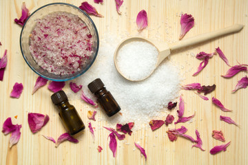 Fototapeta na wymiar omemade scrub for body,sea salt in wooden spoon, aroma oil, rose petals on wooden background. Spa concept.