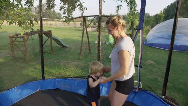 A mother bounces on a trampoline while holding the hands of her young son.  Eventually he falls and her other son piles on top. 4k. Slow motion.