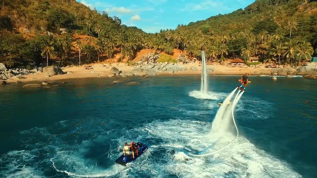 Aerial: Two men flying on flyboard near the beach.