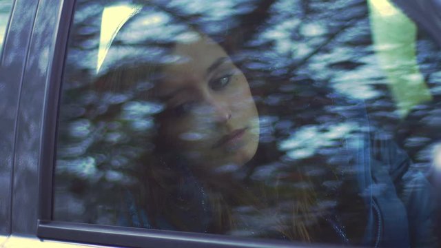 depressed and bored young woman sitting alone in a car: car window reflection