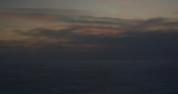 Dark clouds flow over horizon at sunset past snow on sea ice