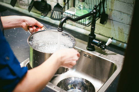 woman housewife in the kitchen. girl collects water from the tap in the pan