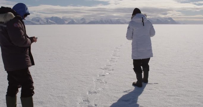 Tourist take pictures of polar bear tracks on sea ice