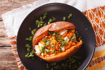 Orange sweet potatoes baked with cream cheese, spices and herb close-up on a black plate. horizontal top view