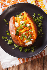 Orange sweet potatoes baked with cream cheese, spices and herb close-up on a black plate. vertical top view
