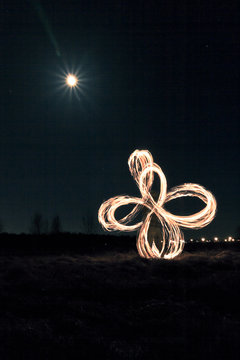 Man is spinning the poi - ropes with the fire, making different installations at night, moon on the background