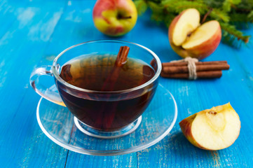 Winter warms festive Vitamin tea with apple and cinnamon on a blue wooden background in a transparent cup of glass.