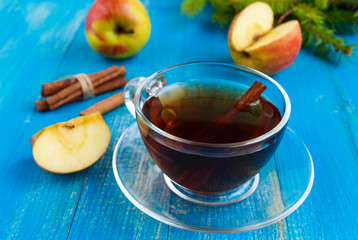 Winter warms festive Vitamin tea with apple and cinnamon on a blue wooden background in a transparent cup of glass.