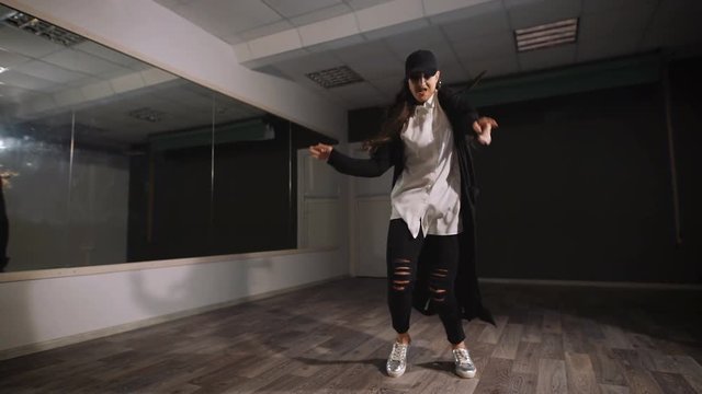 Female dancer in white shirt, black trousers and black cap showing jazz modern dancing. Girl is expressively dancing and professionaly doing elements of streetstyle dance.