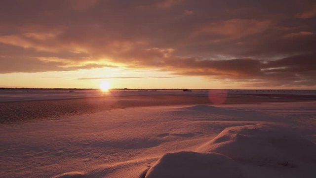 Wide pan of setting sun over icy tundra