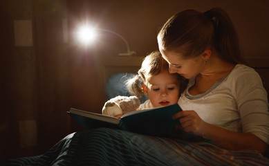 mother and child girl reading a book in bed