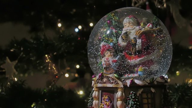 Christmas snow globe ball before blurred background with space for text. Decorating Christmas dome ball before a lit Christmas tree.