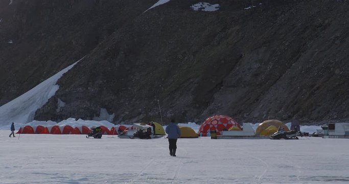Tourist walks towards tent cam on sea ice at base of mountain