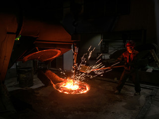 Foundry worker collecting molten metal sample for testing with sparks flying.